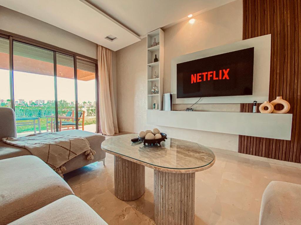 ein Wohnzimmer mit Fernseher und Tisch in der Unterkunft Luxury Apartment in Prestigia Marrakech in Marrakesch