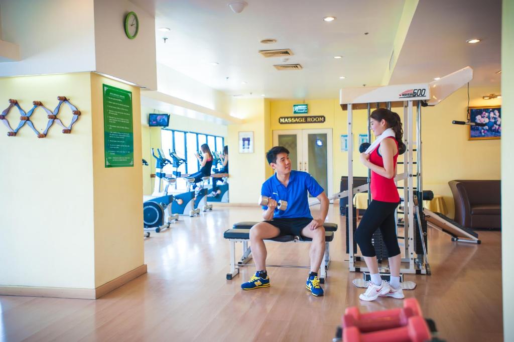 A trainer and guest stand beside a multi-station weight machine in the fitness room.