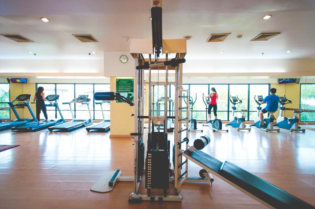 A bright gym contains cardio machines and a central cable-and-weight station.