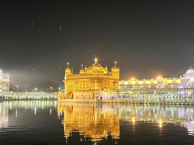 Un templo dorado iluminado con su reflejo en el agua. en Farms View, en Amritsar