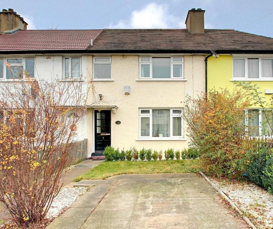 a yellow house with a driveway in front of it at Charming two bedroom house in Northolt