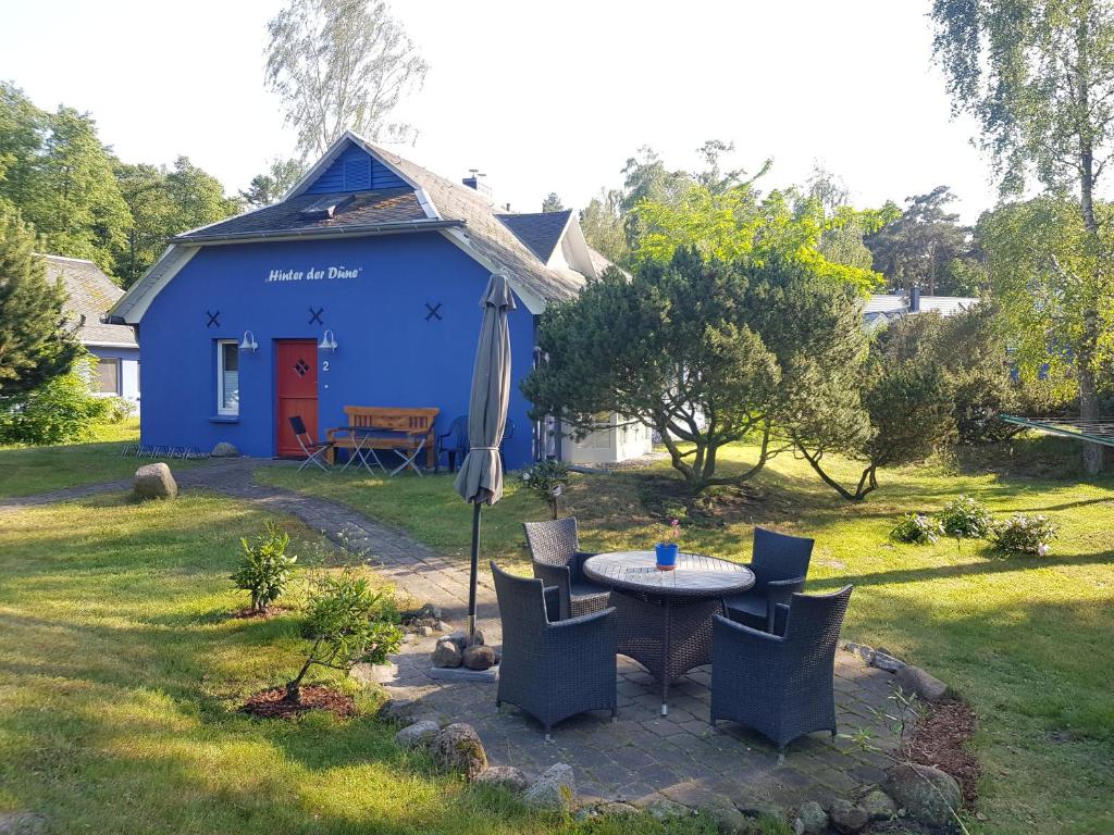 a blue house with a table and chairs and an umbrella at Blaues Strandhaus Hinter der Düne - Erste Reihe - Strand Ückeritz in Ueckeritz