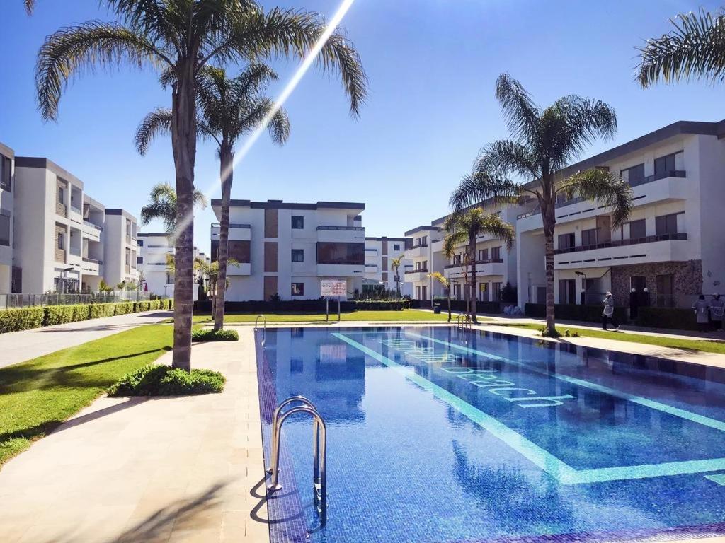 a swimming pool with palm trees and buildings at Eden Prestige in Bouznika