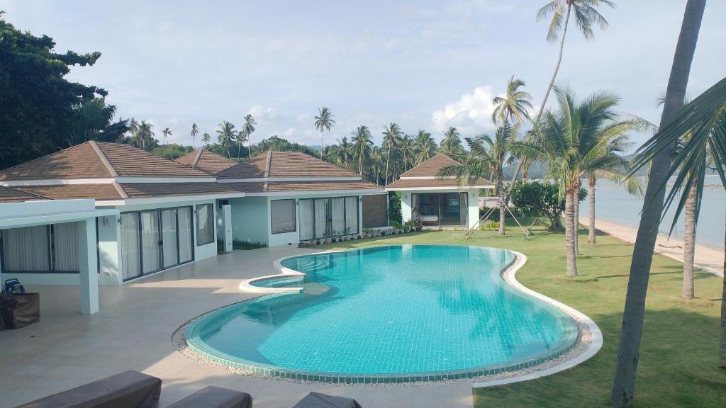a swimming pool in front of a house with palm trees at Baan Tasha in Laem Sor