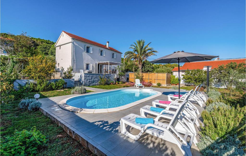 a pool with chairs and an umbrella and a house at Lovely Home In Brbinj With Wifi in Brbinj
