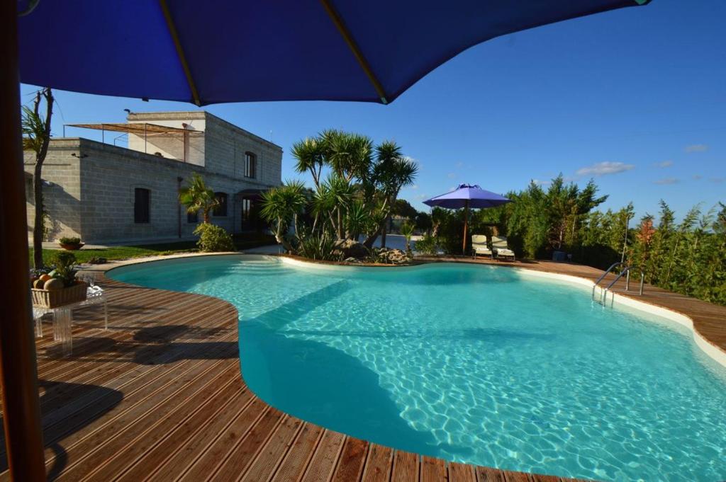 a large swimming pool with an umbrella on a wooden deck at Casina Metrano - Castello Monaci in San Pancrazio Salentino