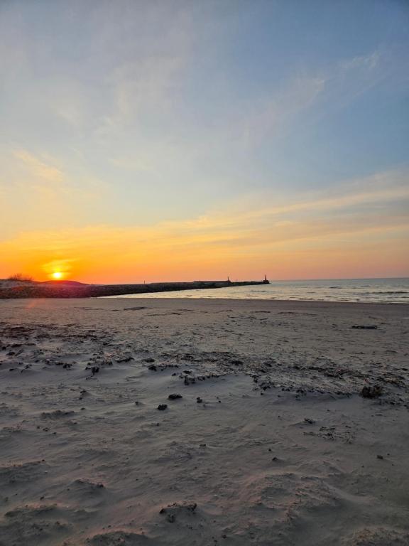 a beach with the sun setting in the distance at Dzintarielas Miera Osta in Pāvilosta