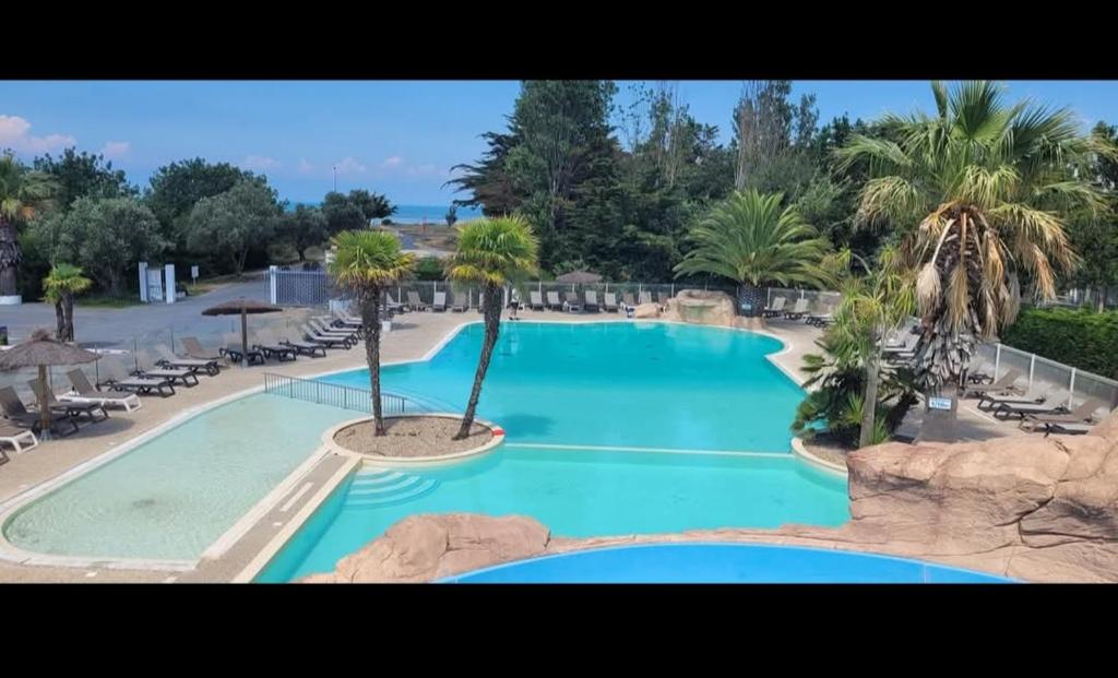 a large swimming pool with palm trees and chairs at Mobilhome neuf 3 chambres Oléron in Saint-Denis-dʼOléron