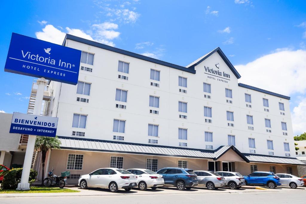 a large white hotel with cars parked in a parking lot at Victoria Inn in Ciudad Victoria