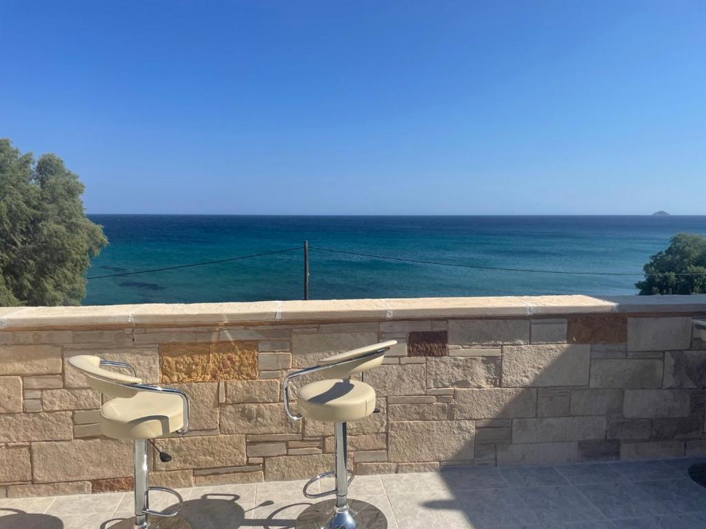 two stools sitting on a stone wall with the ocean at SeaSummerSand Apartment in Chios