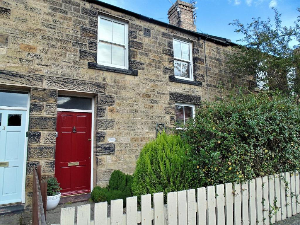 a brick house with a red door and a fence at Oswin Cottge in Alnwick
