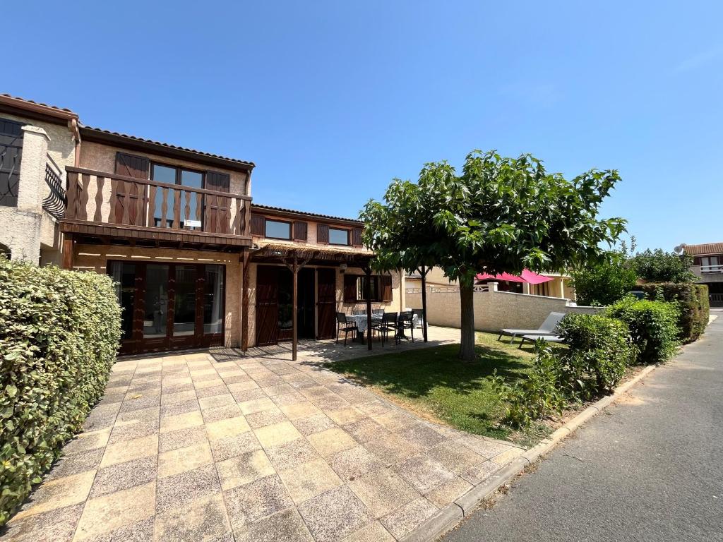 une maison avec une terrasse et un arbre en face de celle-ci dans l'établissement Domaine de vacances à 600m de la plage, villa climatisée 3 chambres 7 couchages WIFI animations piscines en suppléments LRTAMJ36, à Portiragnes