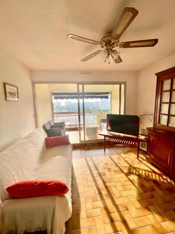 une chambre avec un ventilateur de plafond, un canapé et un piano dans l'établissement Appartement lumineux avec loggia, vue sur le port, CARNON PLAGE, à Carnon-Plage