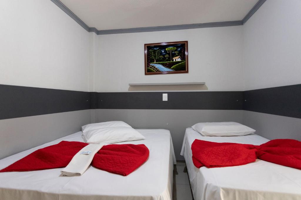two beds in a room with red towels on them at Turis Hotel & Choperia in Dourados