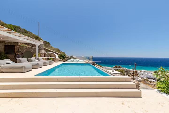 una piscina con sedie e l'oceano sullo sfondo di Eternity Blue Villa a Mykonos Città