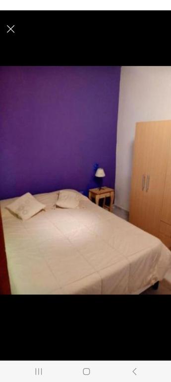a bedroom with a white bed with a purple wall at Cabaña de la flor in El Bolsón
