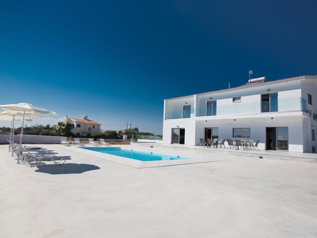 ein großes weißes Gebäude mit einem Pool neben einem Gebäude in der Unterkunft Villa Ioanni Chrysos - Luxury And New 6 Bedroom Protaras Villa in Protaras