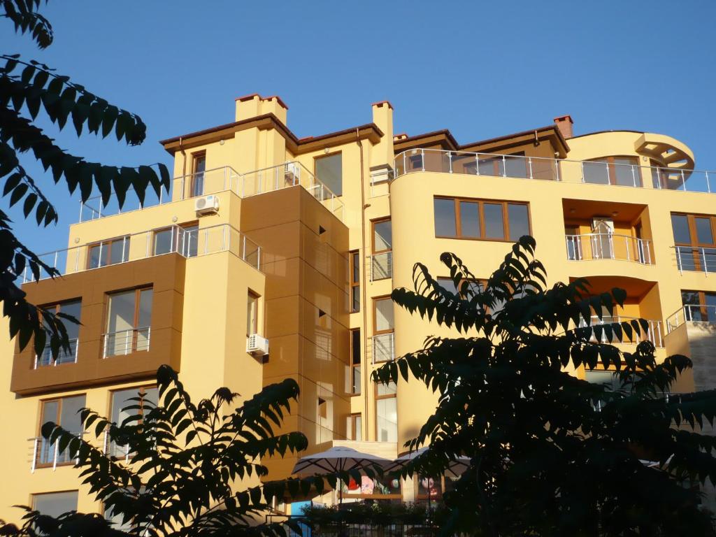 ソゾポルにあるAnteya Serdika Apartmentsの目の前に木が立ち並ぶ高い黄色の建物