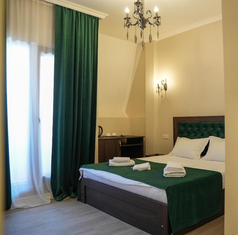 a bedroom with a bed with green curtains and a chandelier at Hotel BABU in Kutaisi