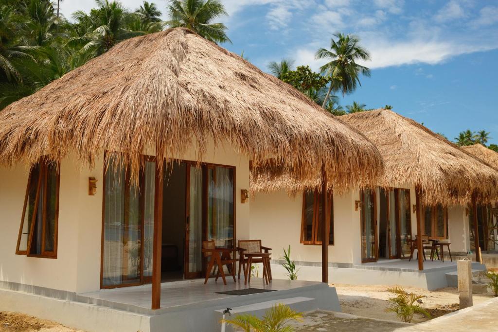 twee hutten met tafels en stoelen ervoor bij Uma Resort Togean in Katupa