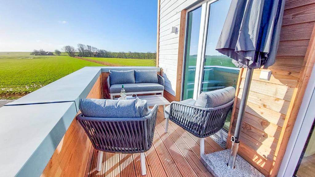 a balcony with two chairs and an umbrella at Deichbude Tossens - Modernes Ferienhaus für 4 Personen in Butjadingen OT Tossens