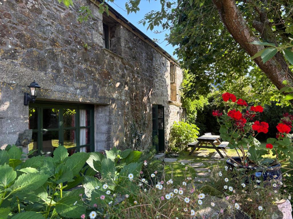 a stone building with a picnic table and red flowers at The Barn, Higher Boden, Manaccan, Helston, Cornwall in Helston