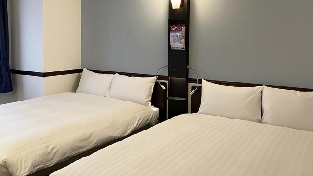 Toyoko Inn Tokyo Akiba Asakusabashi-eki Higashi-guchi في طوكيو: سريرين يجلسان بجانب بعضهما البعض في غرفة