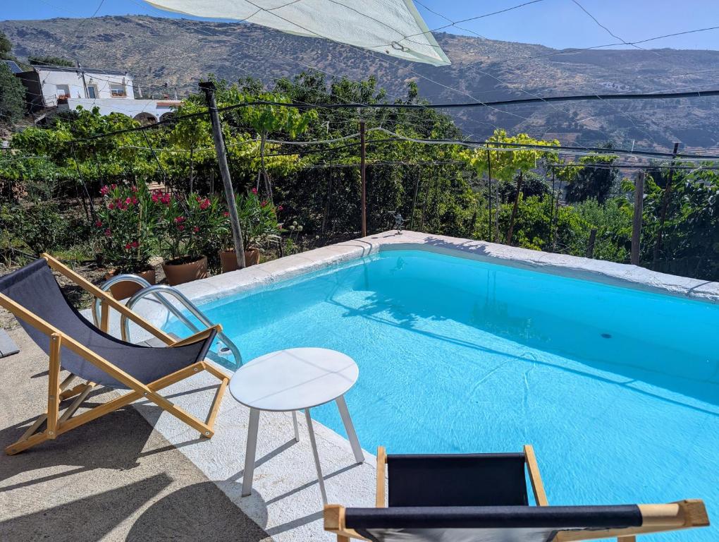 ein Swimmingpool mit einem Stuhl und einem Tisch daneben in der Unterkunft Casa rural para 4 personas, 2 dormitorios y terraza sombreada - El Cortijo Escondido, La Uva in Ohanes