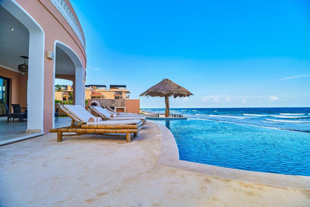 a swimming pool with chairs and an umbrella next to the ocean at Luxury 7 Bedroom Oceanfront Villa at Hacienda Tankah with Infinity Pool & Premium Hospitality in Tulum