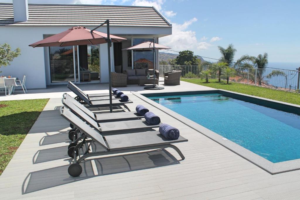 a group of lounge chairs next to a swimming pool at Luxury Calheta Villa Casa Calheta Heights 3 Bedrooms Stunning Sea Views in Calheta