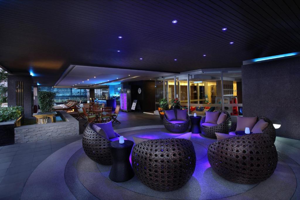 An outdoor-covered lounge uses woven chairs and vivid purple accent lighting.