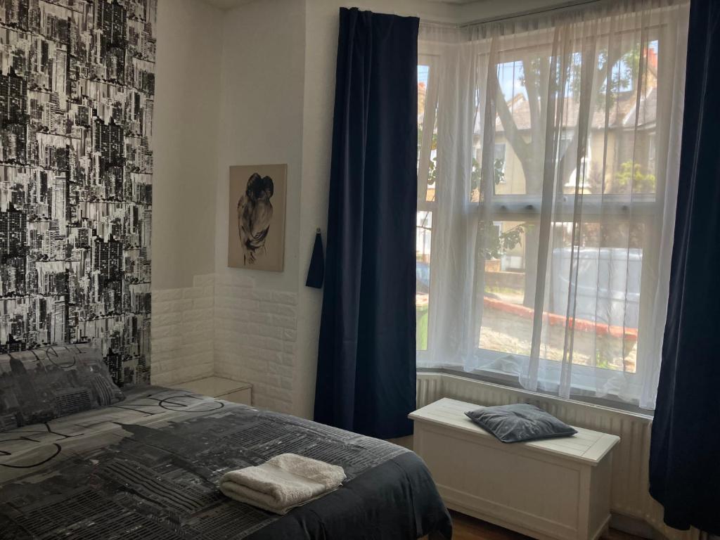 伦敦Comfy rooms. Shared East London Homestay.的一间卧室，有一张床和一扇带蓝色窗帘的窗户
