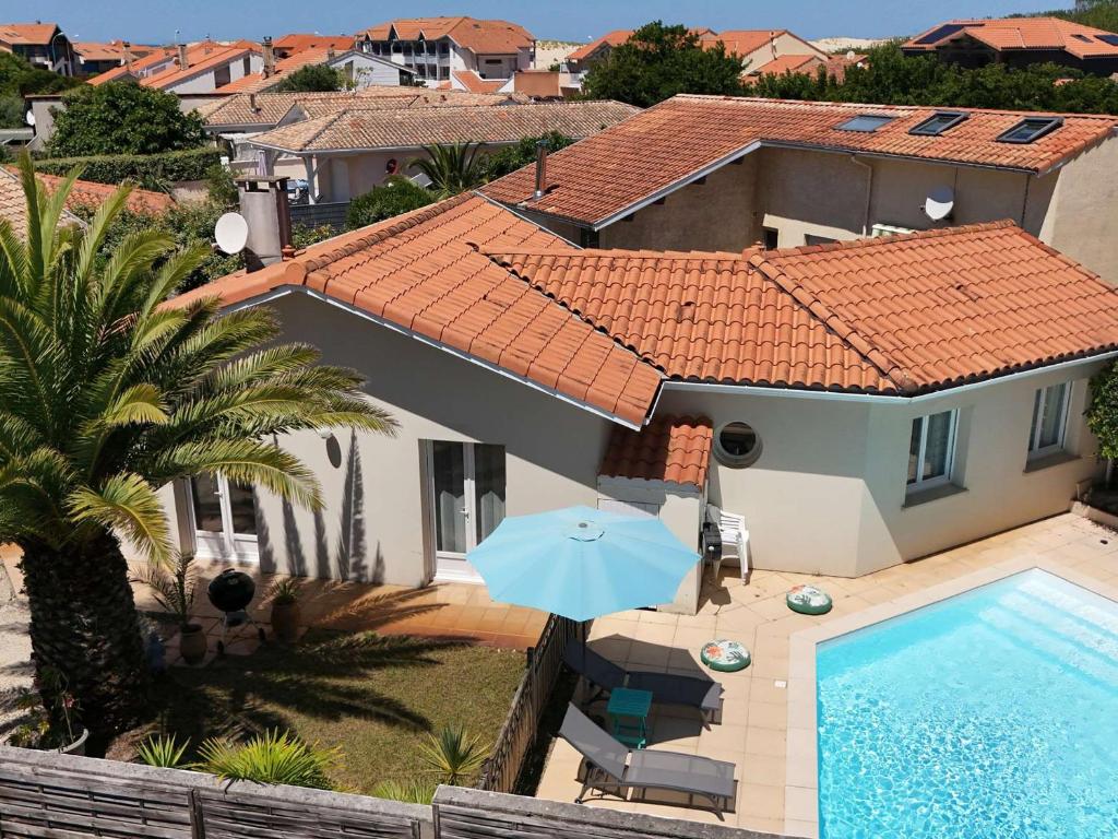 Elle offre une vue sur une maison dotée d'une piscine et d'un parasol. dans l'établissement Charmante villa avec terrasse près de la plage - FR-1-831-11, à Biscarrosse