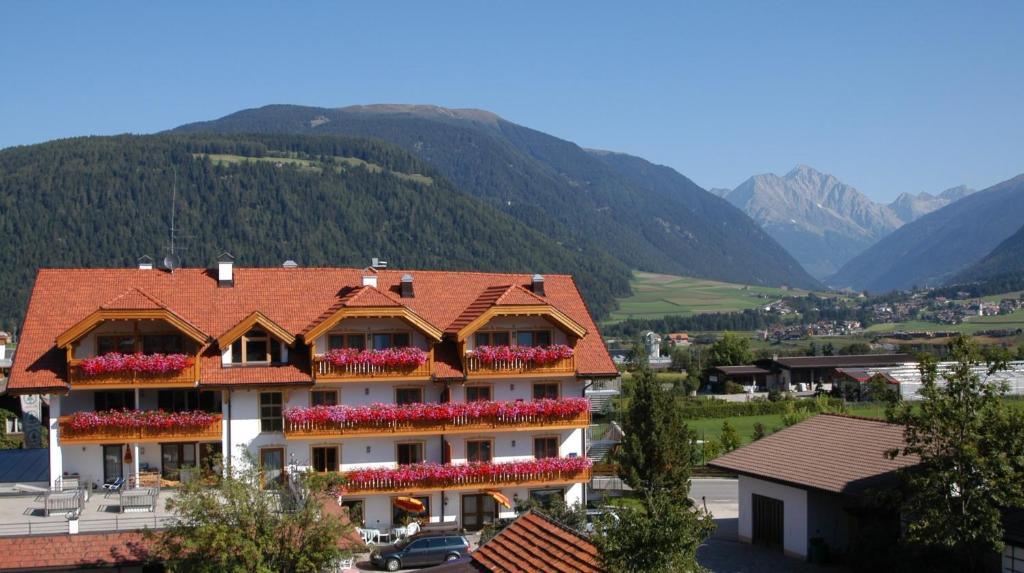 a building with red flowers on the balconies with mountains at Appartments Jägerhof in Valdaora