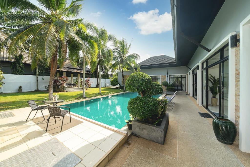 Una piscina con una mesa y sillas al lado de una casa. en Bua Sawan - 4 Bedrooms Pool Villa, en Ban Pak Lak