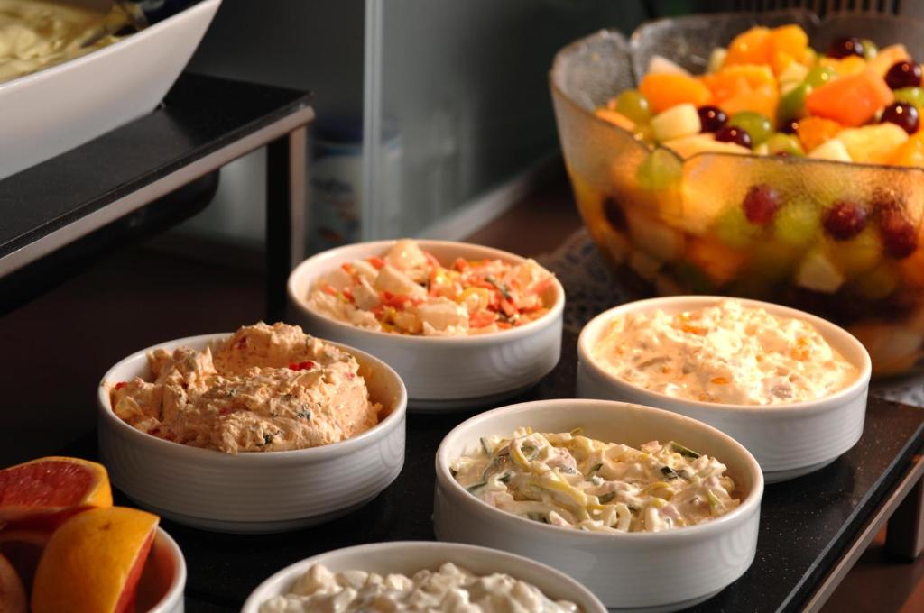 a table with bowls of food and a bowl of fruit at IntercityHotel Bonn in Bonn