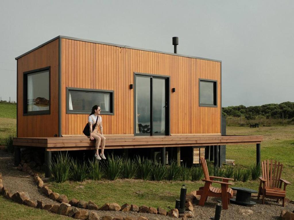 a woman sitting on the deck of a tiny house at É diferente, descubra por quê in Urubici