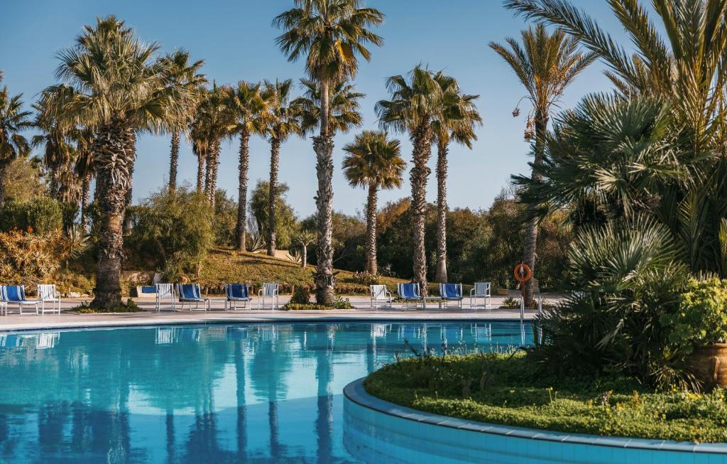 a swimming pool with palm trees and chairs at Verdi Tunis Beach Resort in Gammarth