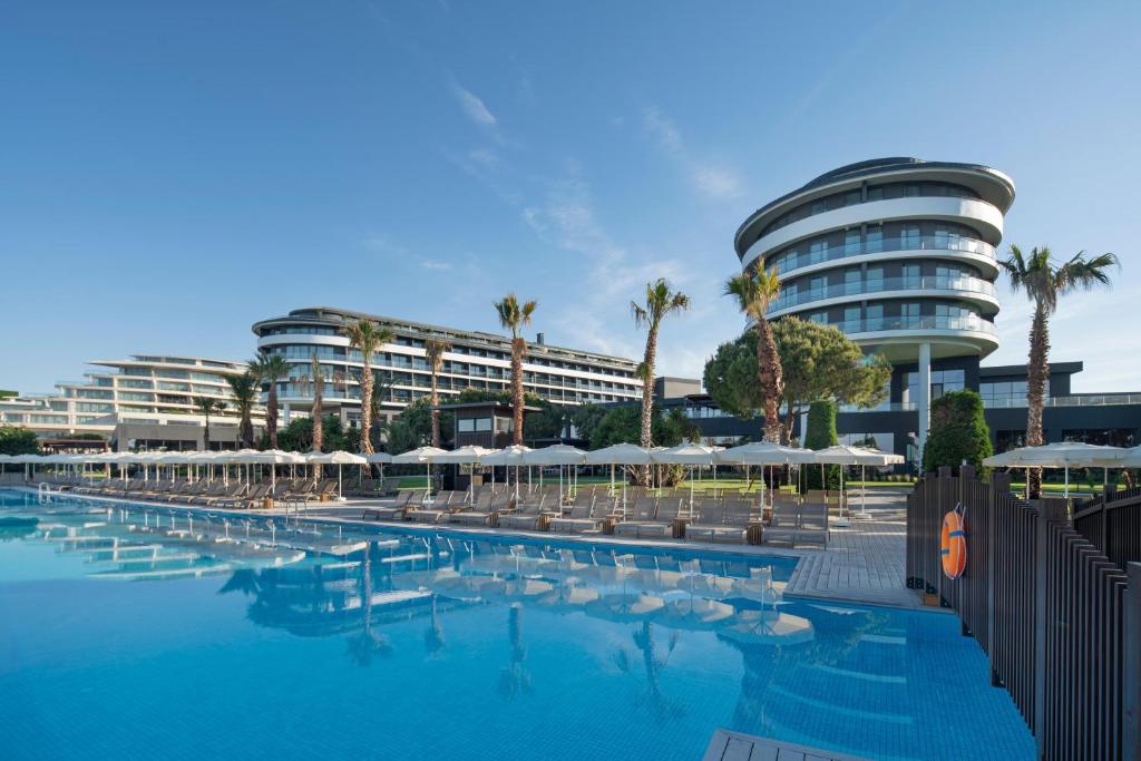 a swimming pool with chairs and umbrellas in front of a building at Voyage Belek Golf & Spa Hotel in Belek