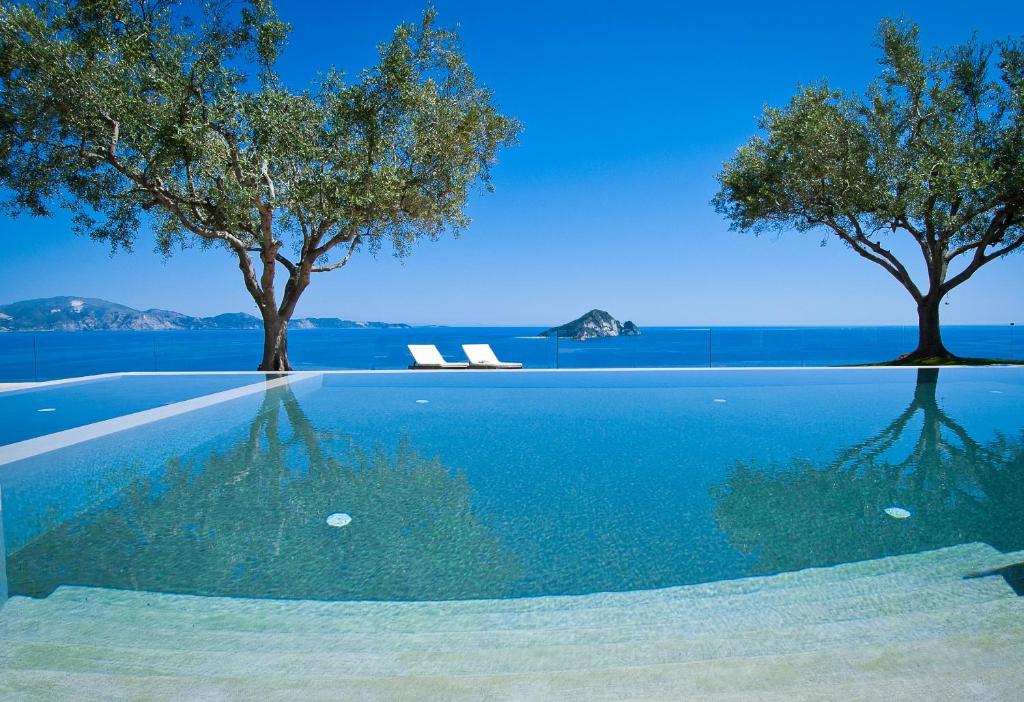 a swimming pool with two trees and blue water at Kymaros Villas in Keri