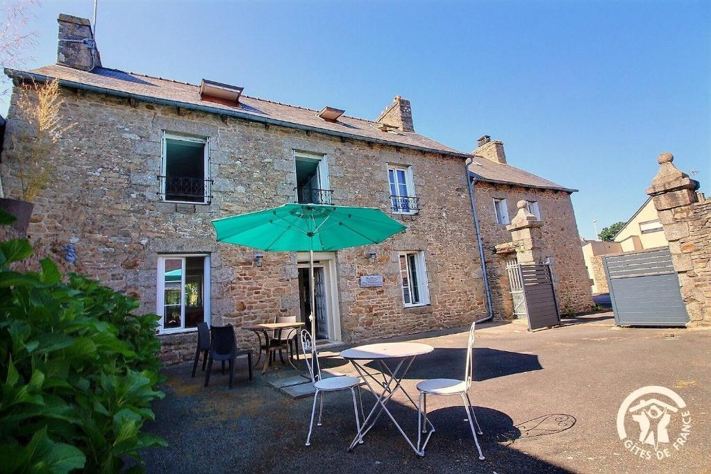 a table and chairs with an umbrella in front of a building at Le clos des hortensias in Plémy