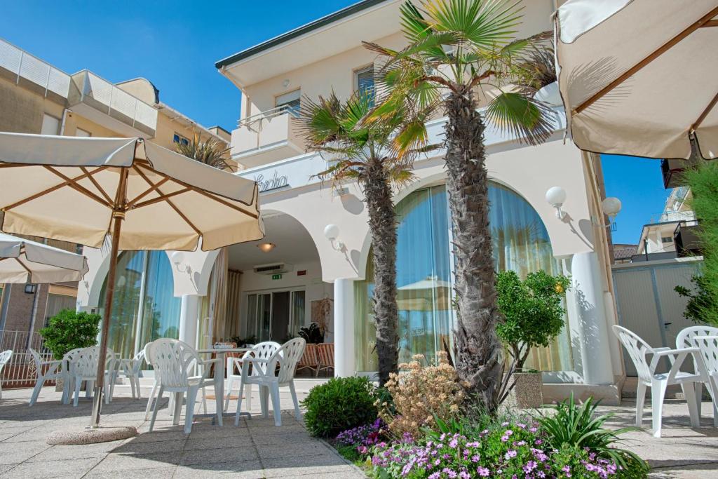 a patio with chairs and umbrellas and palm trees at Hotel Villa Esedra in Bellaria-Igea Marina