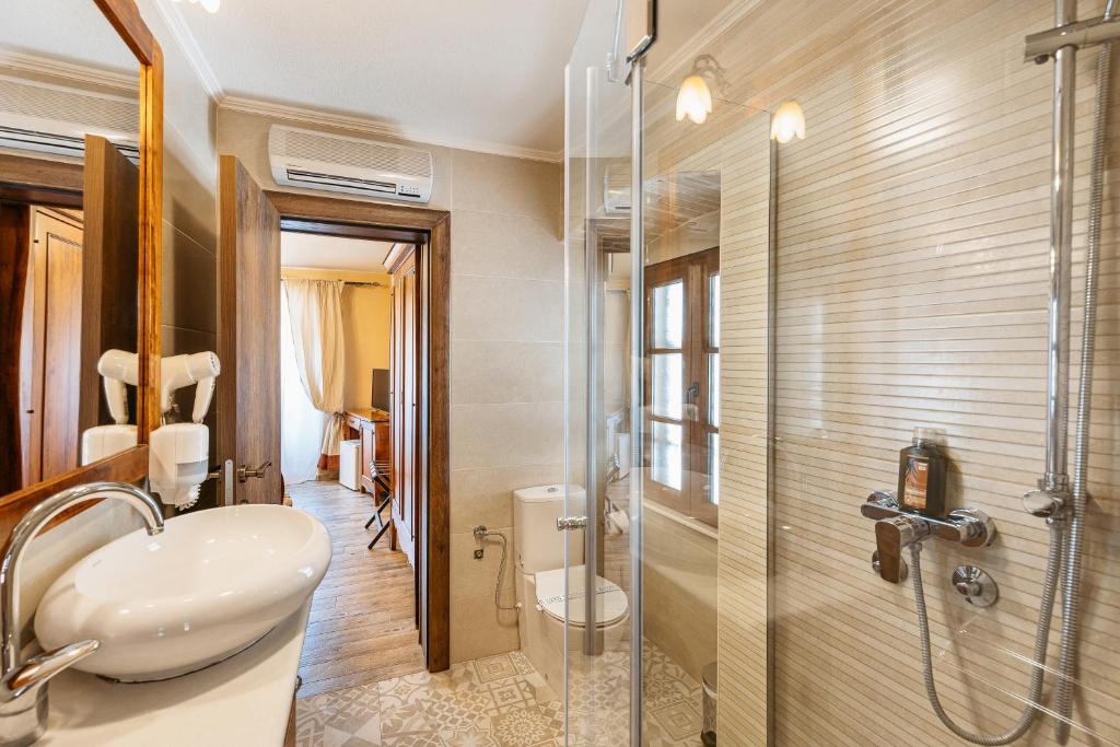 En-suite with glass shower, wall-mounted sink and towel rack, patterned tile floor, AC and wooden doors to seating area at Hotel Monte Cristo in Kotor