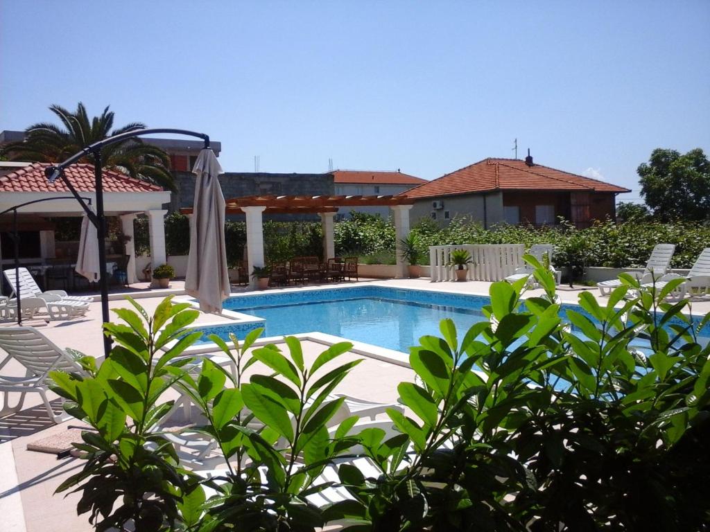 a swimming pool with white chairs and a house at Apartments Zulim in Trogir