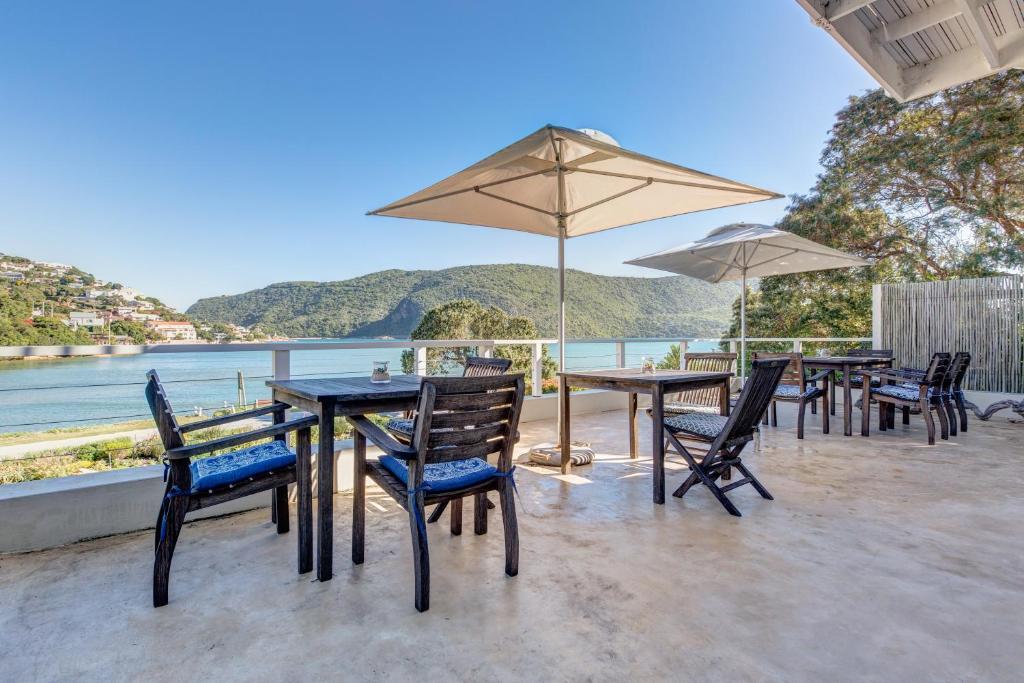 eine Terrasse mit Tischen, Stühlen und einem Sonnenschirm in der Unterkunft Amanzi Island Boutique Hotel in Knysna