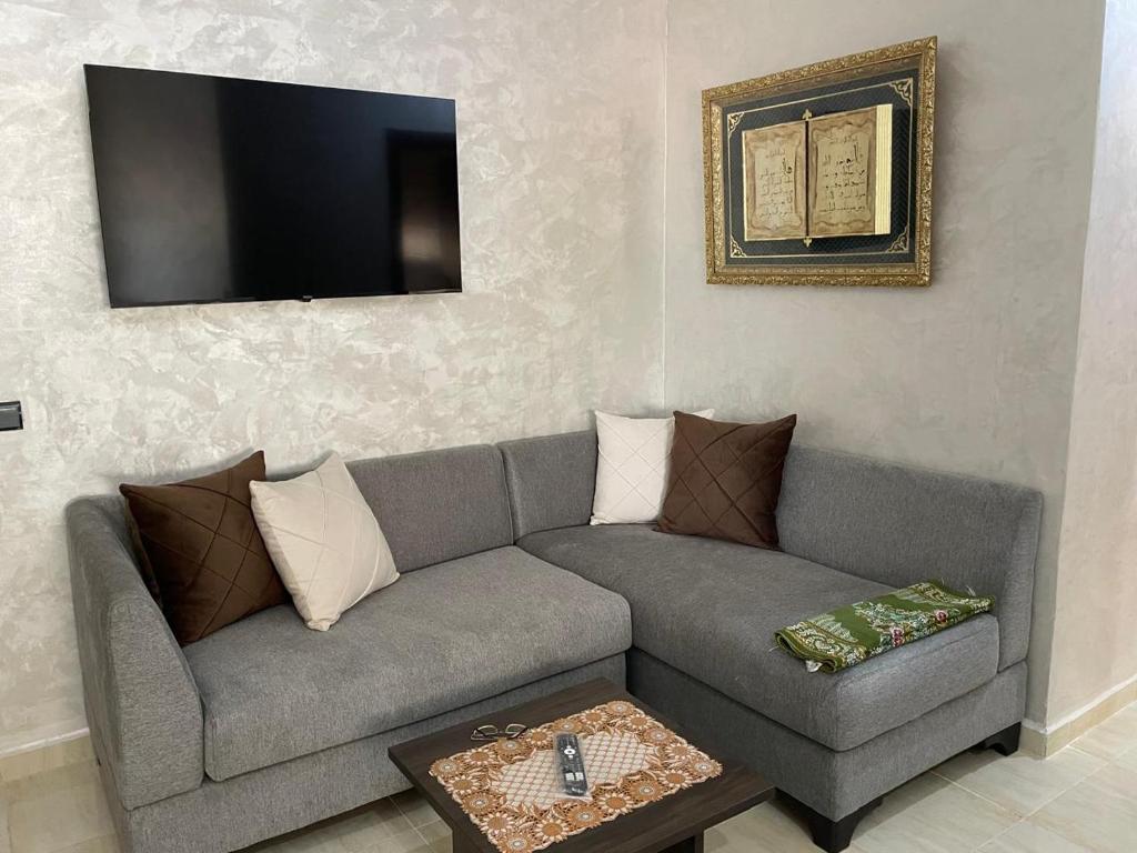 a living room with a gray couch and a flat screen tv at Charmant appartement pour votre séjour a Bouskoura a Casablanca in Bouskoura