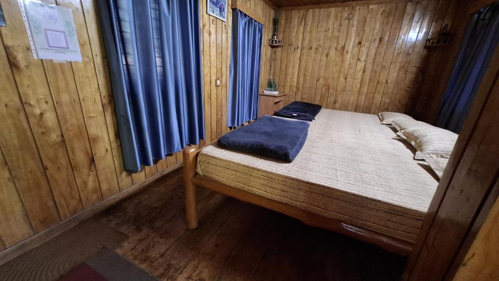 a small bed in a wooden room with blue sheets at Escape Natural Farm Stay - Woodhouse 2 in Kanthalloor