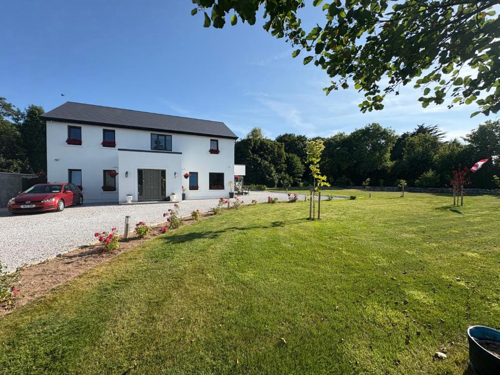 a white house with a car parked in the driveway at Ashlee Lodge, Shanagarry P25K6R6 Near Ballymaloe Cookery School & Garryvoe Hotel in Shanagarry