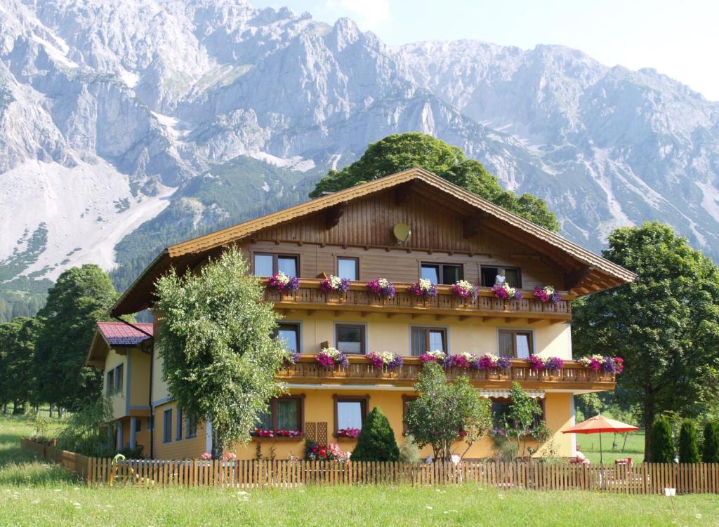 a house with flowers on the balcony in front of mountains at Ferienwohnung Alpenecho in Ramsau am Dachstein