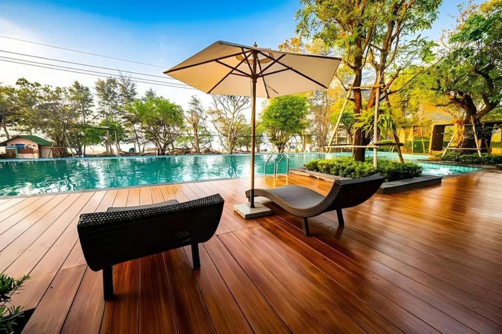 a wooden deck with two chairs and an umbrella at Chatnipa Beach Resort in Klaeng